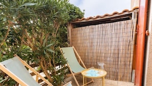 Eine Terrasse mit zwei Liegestühlen, einem kleinen Tisch und einem Bambuszaun.