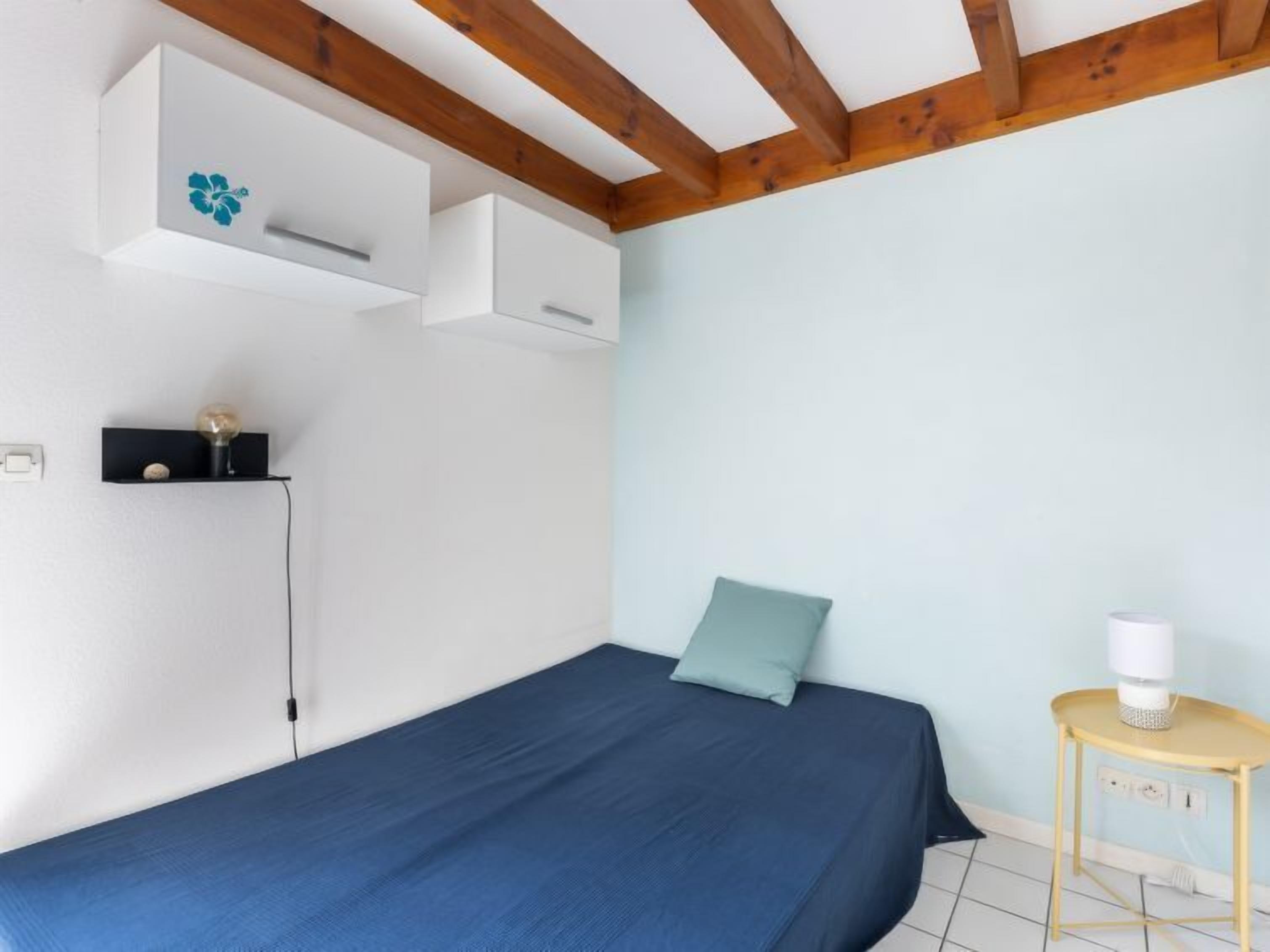 Un dormitorio con una cama individual, una mesita de noche con lámpara y una estantería de pared con un objeto decorativo.