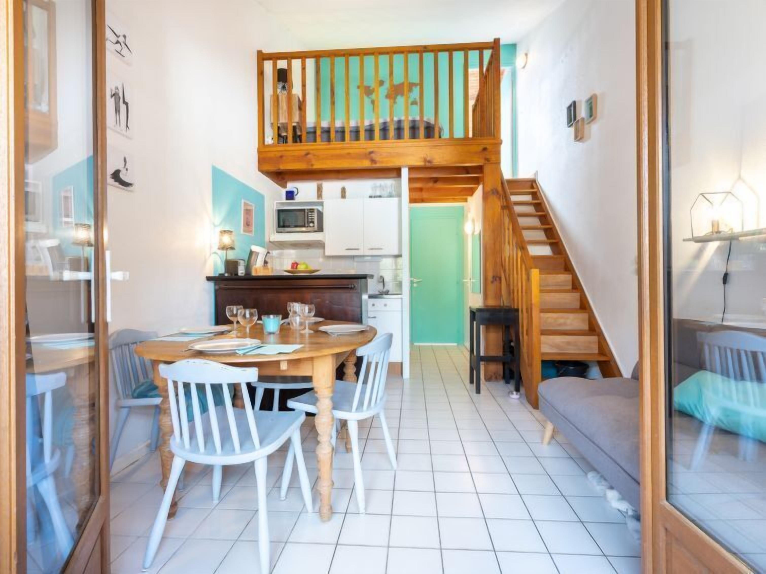 A compact living space with a dining area, kitchen, and a loft bedroom.