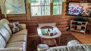 A cozy cabin-style room with a leather sofa, a glass-top coffee table, and a television displaying 'VERDI RIGOLETTO'. - Erätorsa by Interhome (Rautjärvi)