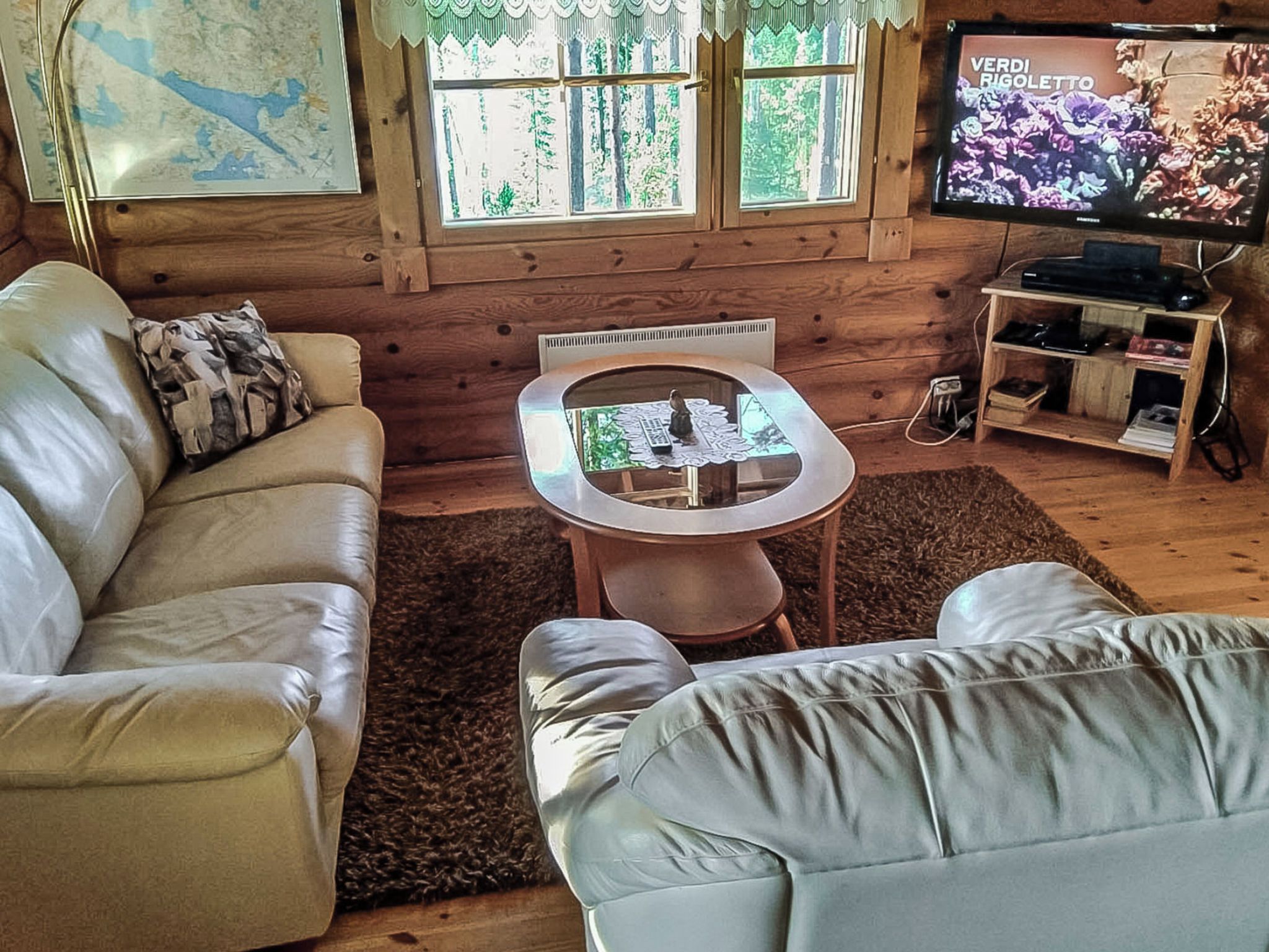 L’intérieur d’un chalet accueillant, avec un canapé en cuir, une petite table et un téléviseur affichant une image florale.