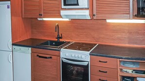 A compact kitchen with wooden cabinets, a microwave, a stove, and a dishwasher. - Erätorsa by Interhome (Rautjärvi)