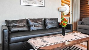 En stue med en sort lædersofa, et træbord med en avis, og en vase med blomster.