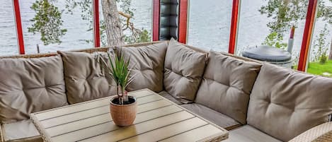 A corner seating area with a woven table and cushioned benches, a potted plant, and a view of a lake through large windows.