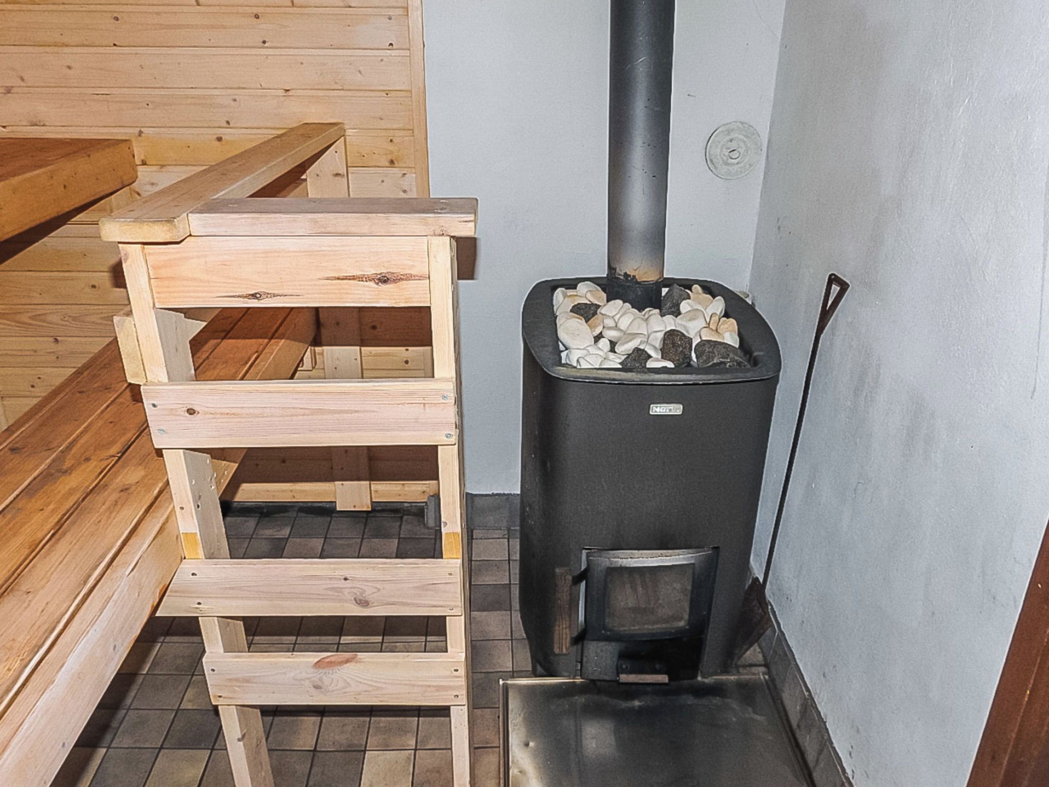 A sauna room with a wooden bench and a black sauna heater.