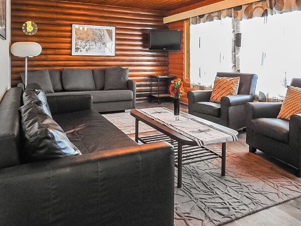 A modern living room with a sofa, armchairs, a coffee table, and a television mounted on the wall.