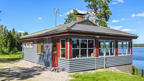 En hytte med grusvej, græsplæne og udsigt til sø.