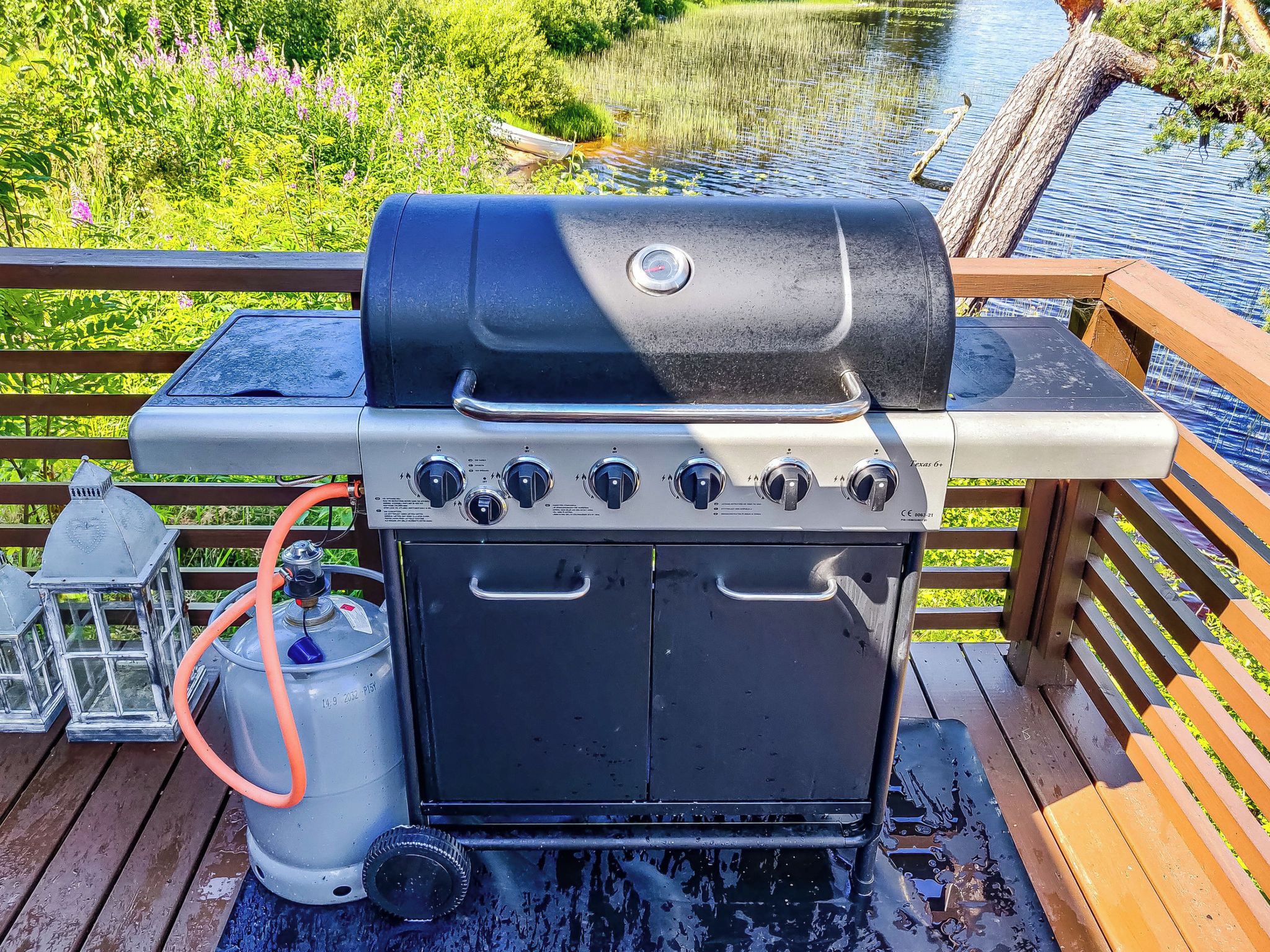 Ein Grill mit Bedienfeld, einer Propangasflasche und einer Holzterrasse mit Geländer.