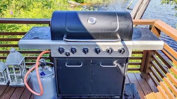 Un barbecue doté d’un panneau de commande, d’une bouteille de propane et d’une terrasse en bois avec une rambarde.