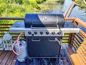 Un barbecue doté d’un panneau de commande, d’une bouteille de propane et d’une terrasse en bois avec une rambarde.