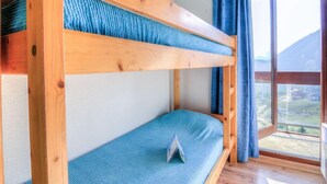 Una cama litera con colchón azul en una habitación con ventana grande y cortinas.