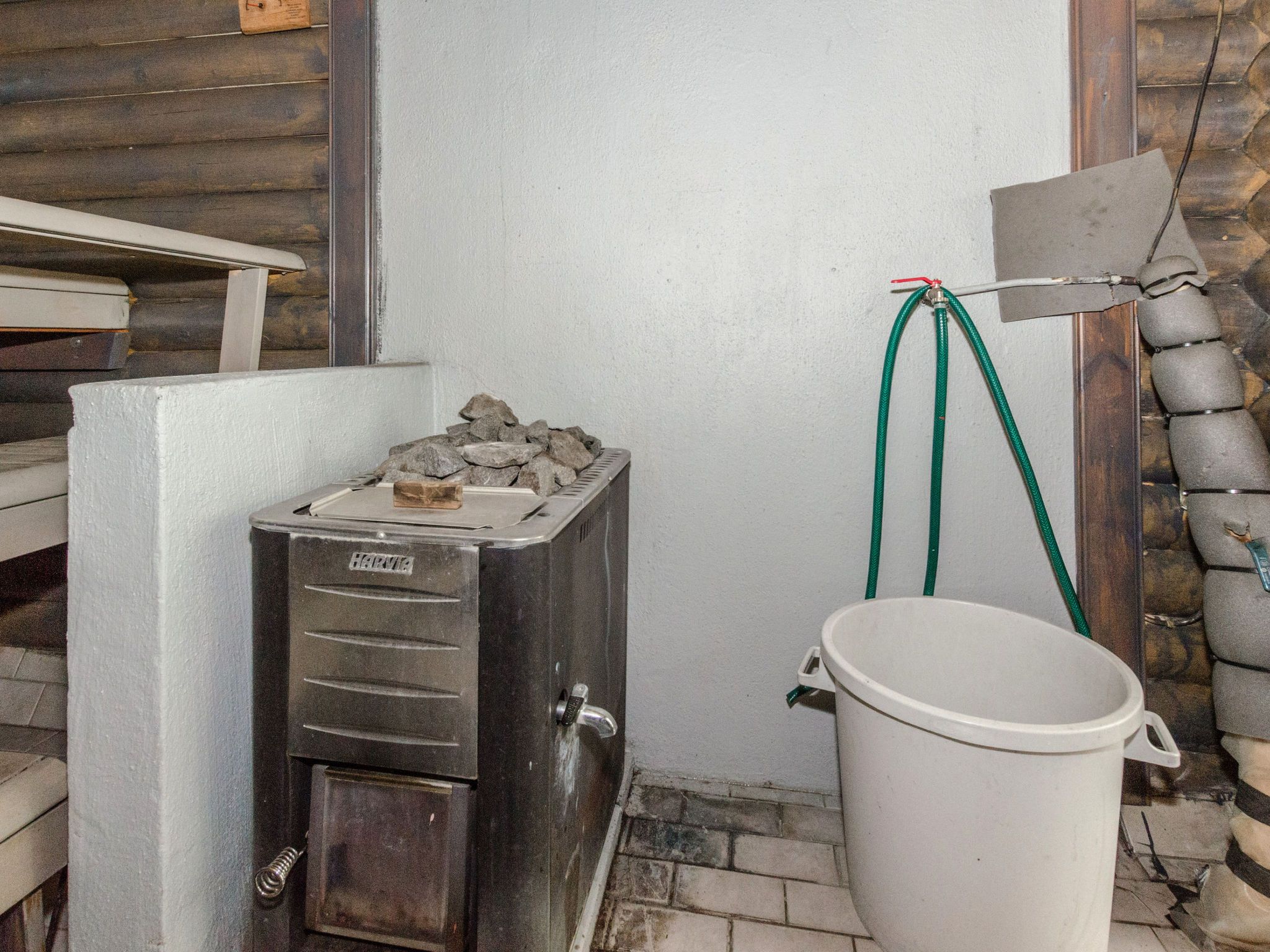 Sauna, jossa on kivipenkki, valkoinen ämpäri ja letku.