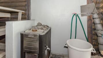 Sauna, jossa on kivipenkki, valkoinen ämpäri ja letku.