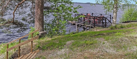 Une terrasse en bois avec une rambarde en métal, donnant sur une étendue d’eau et entourée d’arbres.