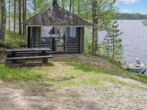A cabin with a hexagonal roof, a picnic table, and a boat docked by the water.