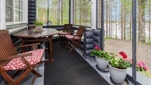 A covered outdoor seating area with a table and chairs, large windows, and potted plants. - Hatun huilaus by Interhome (Ilomantsi)