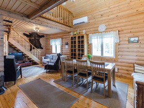 A log cabin interior with a dining area, a sofa, a television, and a staircase.