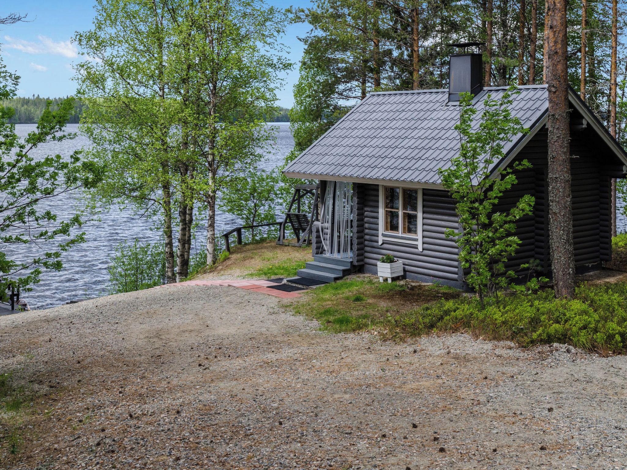 A cabin with a gravel driveway, a wooden deck, and a view of a lake.