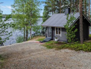 A cabin with a gravel driveway, a wooden deck, and a view of a lake.