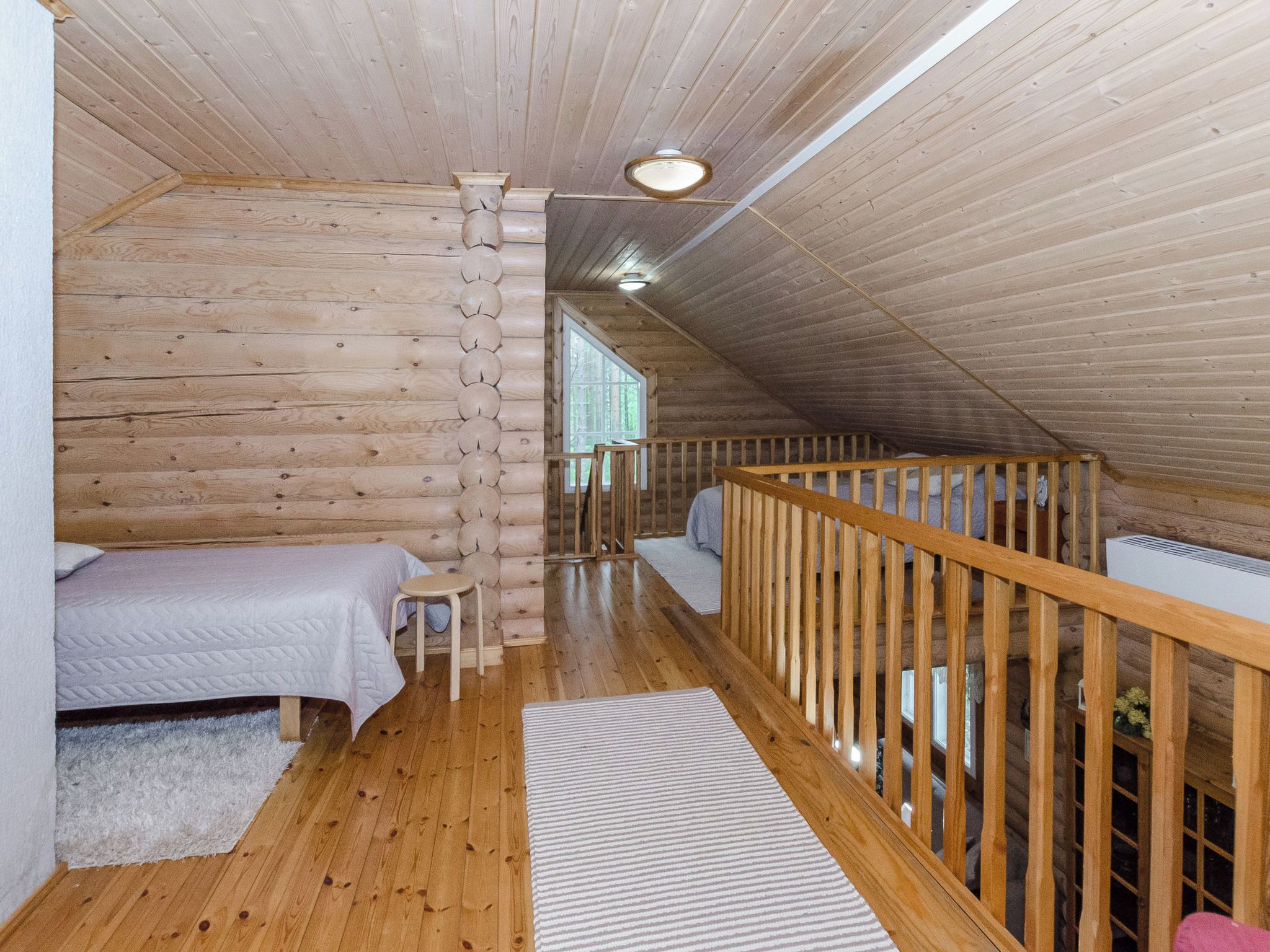 A log cabin bedroom with two beds, a wooden railing, and a window.