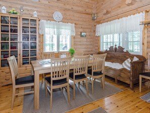 Puinen mökki, jonka sisustuksessa on ruokapöytä, tuoleja, sohva ja lasiovilla varustettu kaappi.