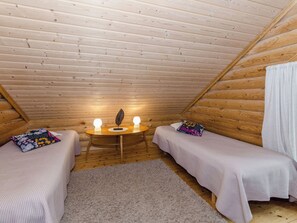Un dormitorio acogedor en el ático, con dos camas individuales, una mesita con dos lámparas y techo de madera.