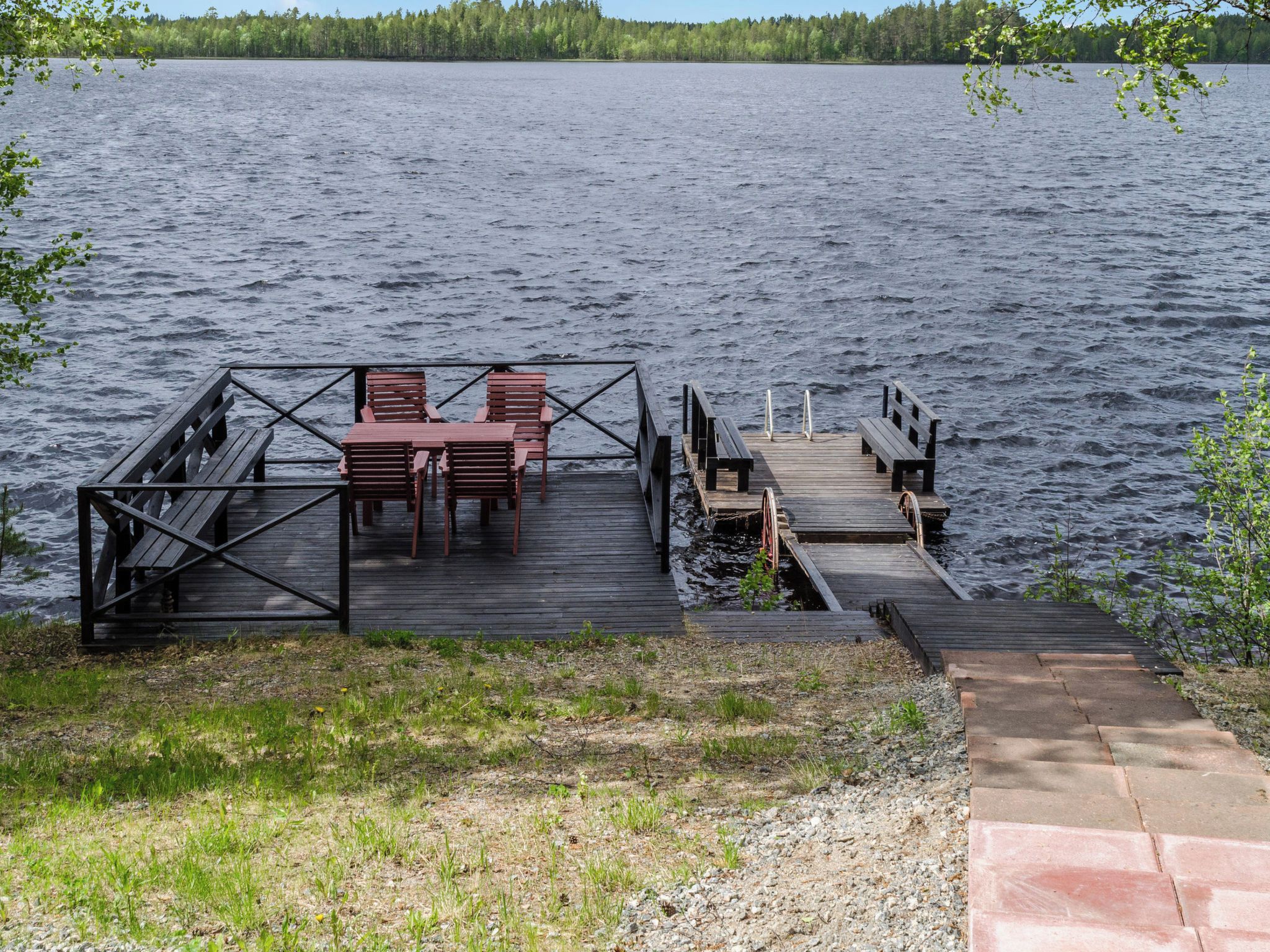 A wooden dock extending into a lake with a seating area and a small bridge.
