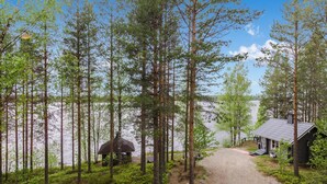 A cabin with a gravel path leading to it, surrounded by tall trees and a lake. - Hatun huilaus by Interhome (Ilomantsi)