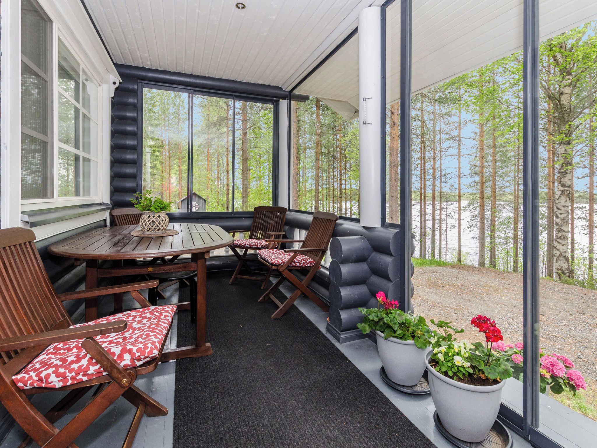 A covered outdoor seating area with a table and chairs, potted plants, and a view of a forest.
