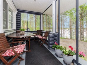 Un espacio de estar al aire libre cubierto con una mesa, sillas, plantas en macetas y vistas a un bosque.