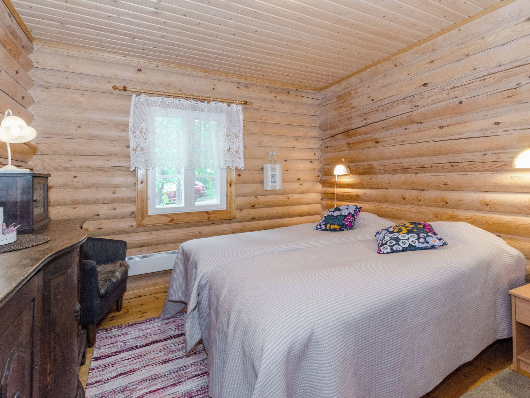 Una camera in una baita di legno, con un letto, una scrivania e una finestra con tende in pizzo.