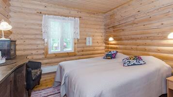 Una camera in una baita di legno, con un letto, una scrivania e una finestra con tende in pizzo.