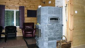 A cozy living room with a stone fireplace, wooden walls, and a comfortable seating area. - Kärkelä by Interhome (Kiuruvesi)