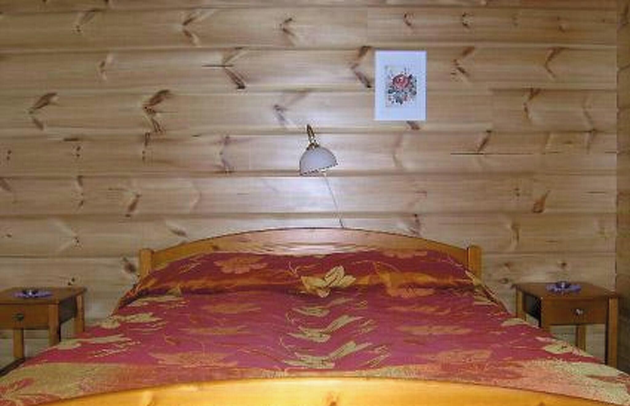 Una habitación con paneles de madera, una cama, una mesita de noche y una lámpara fijada a la pared.