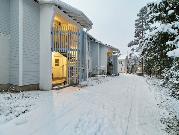 A snow-covered residential area with a house featuring a visible staircase and a gated entrance.