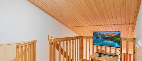 A wooden interior with a television on a stand, a wooden railing, and a ceiling light.