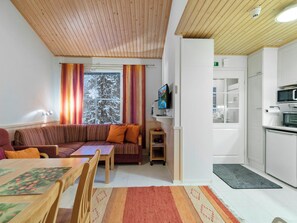 A modern living room with a wooden ceiling, a sofa, a TV, and a kitchen area with a microwave.