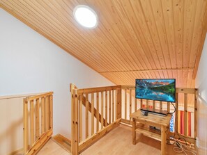A wooden interior with a television on a stand, a wooden railing, and a ceiling light.