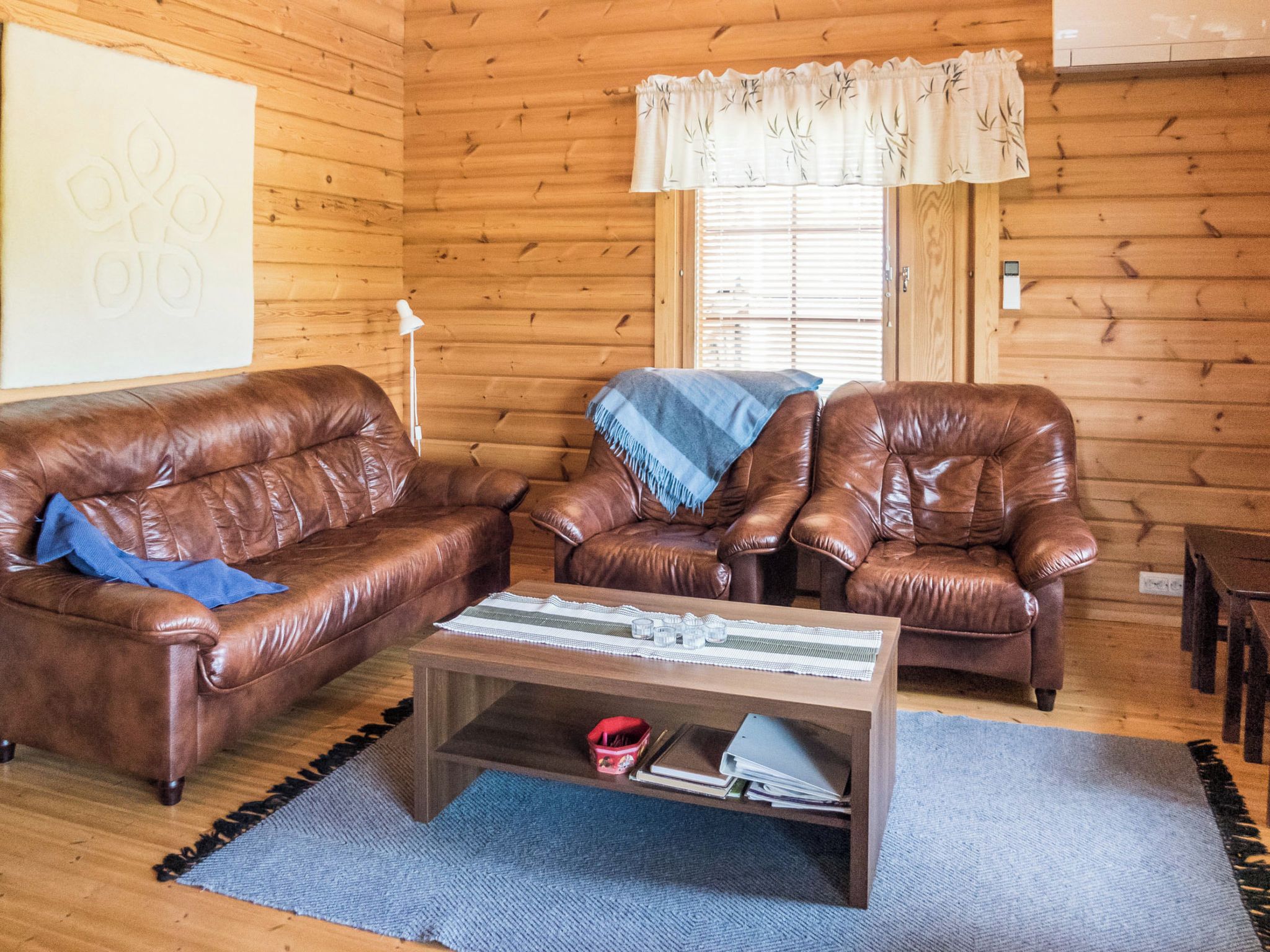 A cozy living room with two brown leather sofas, a wooden coffee table, and a window with blinds.