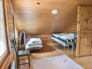 A small, wooden-paneled room with two beds, a chair, and a door.