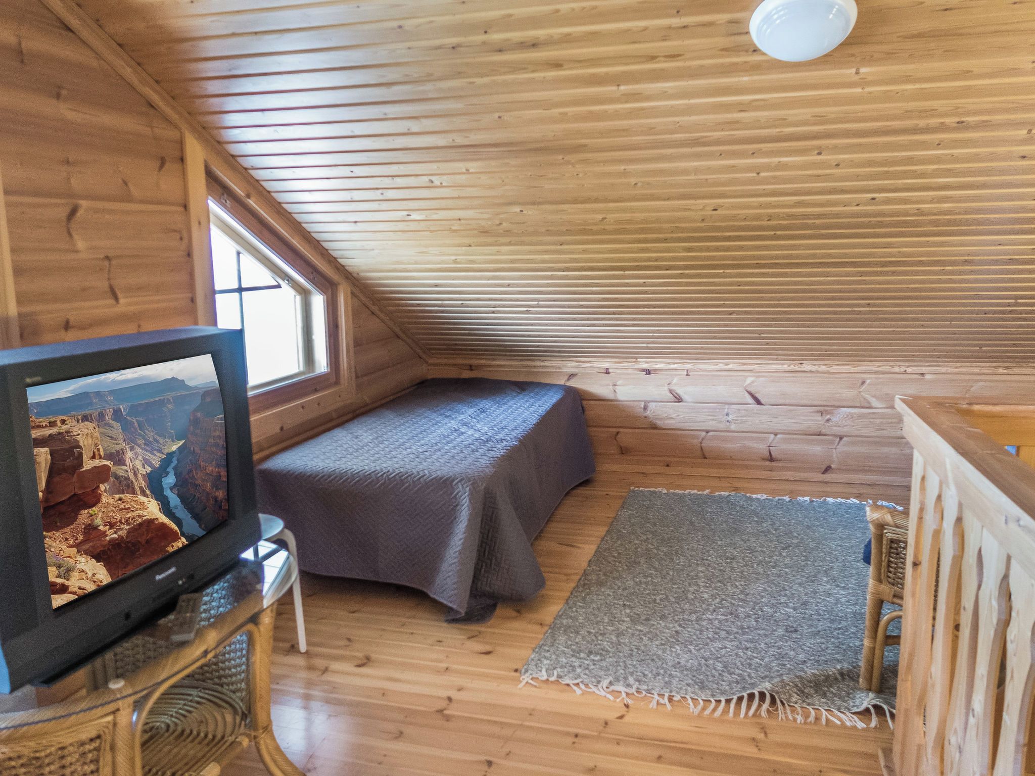 A small, wooden room with a bed, a television, and a window.