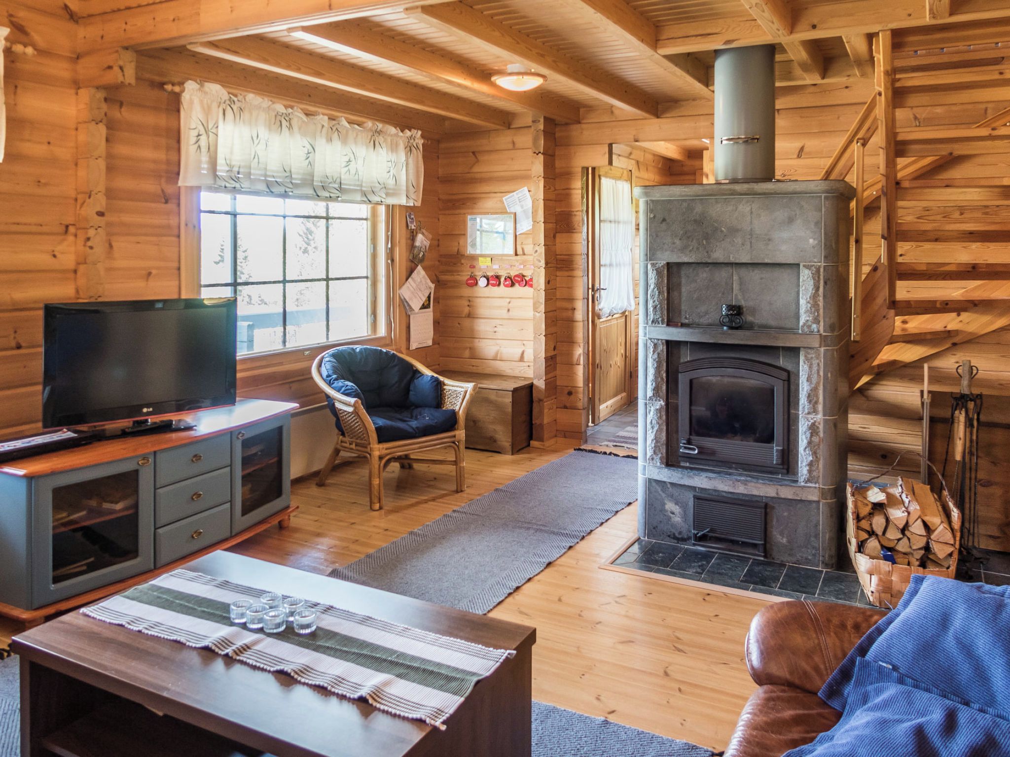 A log cabin interior with a stone fireplace, wooden furniture, and a television on a cabinet.