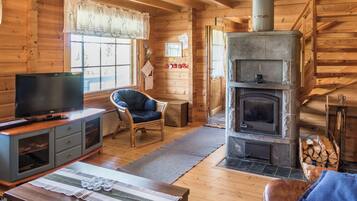 A log cabin interior with a stone fireplace, wooden furniture, and a television on a cabinet.