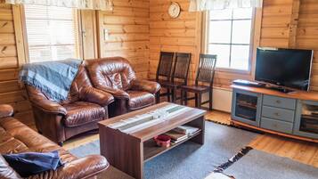 A cozy cabin interior with leather sofas, a wooden coffee table, a TV, and a clock on the wall.