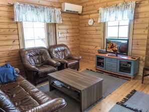 A cozy cabin interior with wooden walls, a leather sofa, a coffee table, and a television on a cabinet.