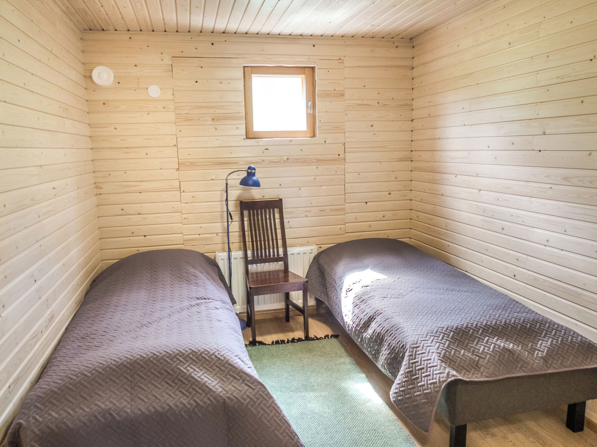 A small, single-room cabin with two beds, a chair, a desk, and a window.
