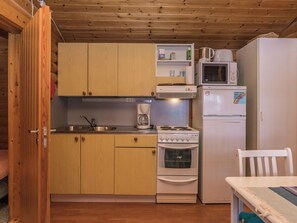 A compact kitchen with wooden cabinets, a microwave, a stove, and a refrigerator. - Länsiranta by Interhome (Punkaharju)