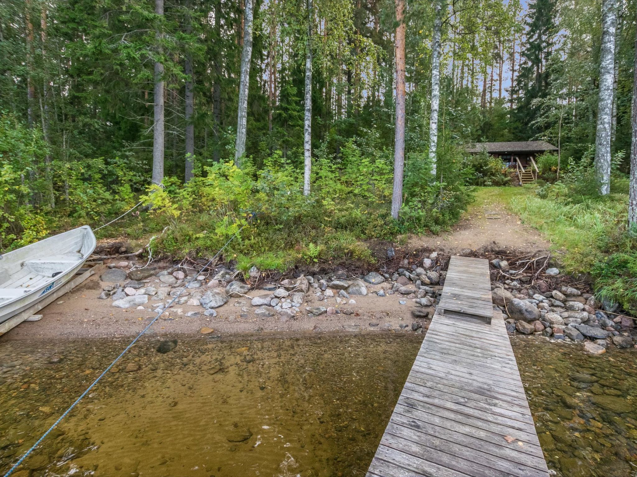 Puinen laituri, joka ulottuu metsäiselle alueelle, ja taustalla näkyy pieni mökki.