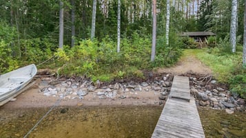 Puinen laituri, joka ulottuu metsäiselle alueelle, ja taustalla näkyy pieni mökki.