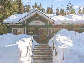 A wooden lodge with a snow-covered roof, a front entrance, and a staircase leading up to the door.
